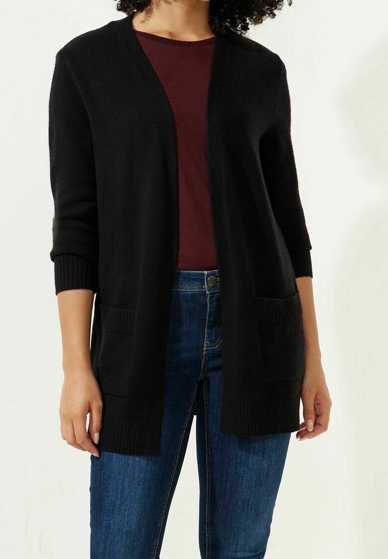 Cardigan noir avec une coupe décontractée, décolleté en V et manches longues. Caractéristiques de poignets côtelés et de deux poches avant, porté sur un haut bordeaux.