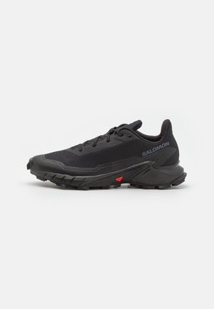 Baskets de trail running noires avec une tige respirante, un tissu texturé, un accent rouge sur la semelle et un profil de semelle agressif pour l'adhérence.