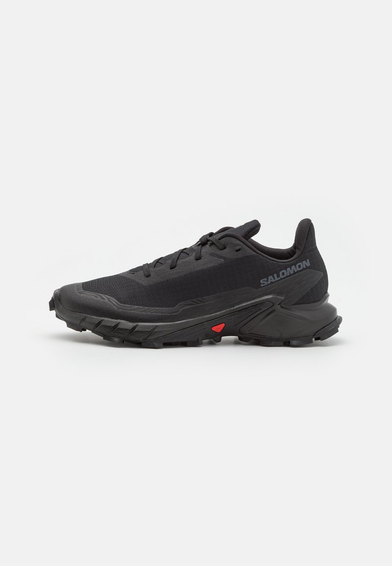 Black trail running shoes featuring a breathable upper, textured fabric, red accent on the sole, and aggressive tread for grip.
