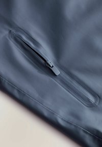 Gros plan sur une poche partiellement ouverte d'une veste imperméable bleue avec une fermeture éclair étanche élégante sur un tissu lisse.