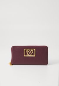 Burgundy textured leather wallet with a gold-tone logo plaque, zip closure, and a small charm at the zipper pull.
