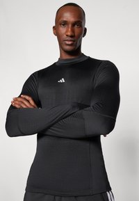 Schwarzes langärmliges Sportoberteil aus dehnbarem Material mit tailliertem Schnitt. Verfügt über ein kleines weißes Adidas-Logo auf der Brust.