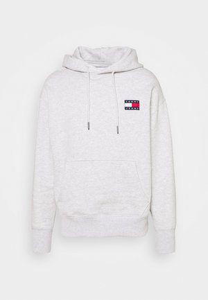 Jasnoszara bluza z kapturem typu pullover z przednią kieszenią, sznurkami i małym logo "Tommy Jeans" na lewej piersi.