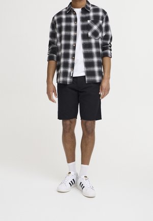 Chemise en flanelle à carreaux noirs et blancs, t-shirt blanc, shorts noirs et baskets blanches avec des rayures noires. Texture unie ; fermeture à boutons.