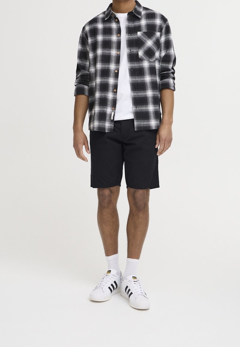 Chemise en flanelle à carreaux noirs et blancs, t-shirt blanc, shorts noirs et baskets blanches avec des rayures noires. Texture unie ; fermeture à boutons.