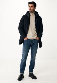 Černá péřová bunda s kapucí, zipovým předním zapínáním a dvěma náprsními kapsami. Béžový rolák, modré džíny s ohrnutými rukávy a černé kotníkové boty.