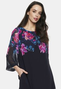 Granatowa sukienka w kwiatowy wzór w odcieniach różu i niebieskiego, z przezroczystymi rękawami, okrągłym dekoltem oraz bocznymi kieszeniami dla większej funkcjonalności.