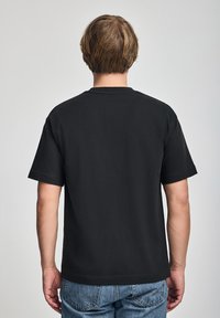 Svart bomullströja med rund hals, korta ärmar och en avslappnad passform, med en enkel design utan grafik.