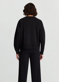 Sweat-shirt noir avec manches raglan, poignets et ourlet côtelés, associé à un pantalon large noir coordonné. Texture unie, design minimaliste.