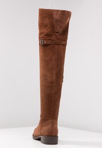 Brązowe kozaki zamszowe za kolano na płaskim obcasie, z ozdobnym paskiem i klamrą u góry. Gładka faktura, dopasowany fason.