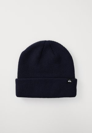 Navy blue knitted beanie with a folded cuff and small black tag featuring a white logo on the cuff, on a plain light background.