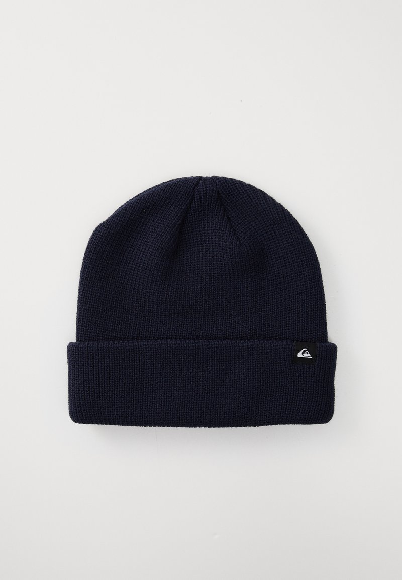 Navy blue knitted beanie with a folded cuff and small black tag featuring a white logo on the cuff, on a plain light background.