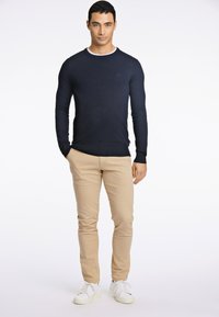 Granatowy sweter z długim rękawem o prążkowanej fakturze, zestawiony z jasnobeżowymi chinosami i białymi trampkami. Prosty, nowoczesny design z okrągłym dekoltem.