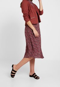 Red floral dress with a flared hem, paired with a cropped maroon jacket. Black strappy sandals complete the outfit. Smooth fabric texture.