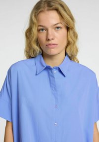 Camicia azzurra a maniche corte realizzata in un tessuto liscio, con chiusura a bottoni e colletto classico.