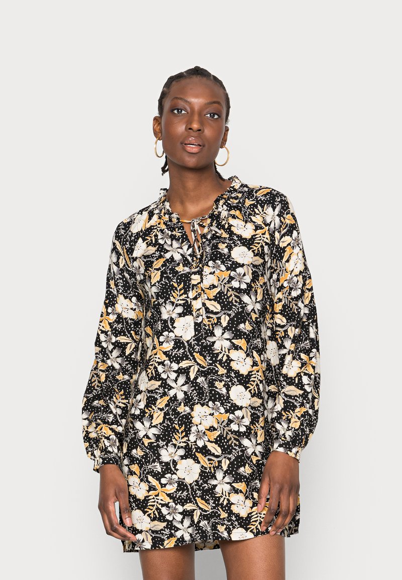 Vestido floral com fundo preto, apresentando padrões de flores amarelas e brancas, um decote com babados e mangas longas bufantes.