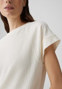 Witte textuur top met korte mouwen en een ronde halslijn, met een subtiel ruitpatroon en raglanmouw ontwerp.