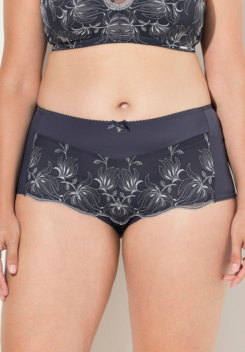 Mutandine a vita alta in blu navy con ricami floreali e bordo in pizzo, con un piccolo dettaglio a fiocco in vita e una texture liscia e morbida.