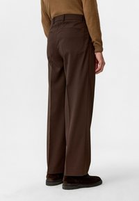 Bruine wijde broek van een zachte stof. Heeft een rechte taille, twee achterzakken en een tailleband met riemlussen.
