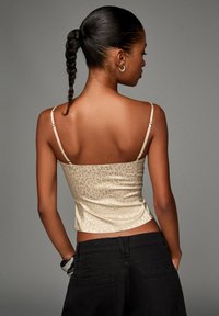 Beige leopard-print fitted top with thin straps, textured fabric, and a cropped design, paired with black high-waist pants.