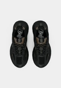 Černé sportovní tenisky s texturovaným síťovaným svrškem, zaobleným tvarem, silnou podrážkou a kontrastními hnědými akcenty. Na jazyku jsou ozdobeny logem.