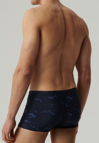 Męskie kąpielówki w ciemnoniebieskim materiałach z wzorem, charakteryzujące się niskim stanem i gładką fakturą, z delikatnymi akcentami falistymi.