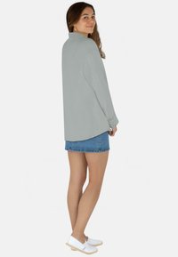 Hellgraues Langarmshirt mit lässigem Schnitt und Knopfmanschetten, kombiniert mit einem Jeans-Minirock und weißen Slipschuhen.