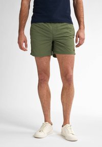 Shorts da bagno verdi realizzati in tessuto leggero, con un design semplice, indossati con sneakers bianche e una maglietta blu navy.