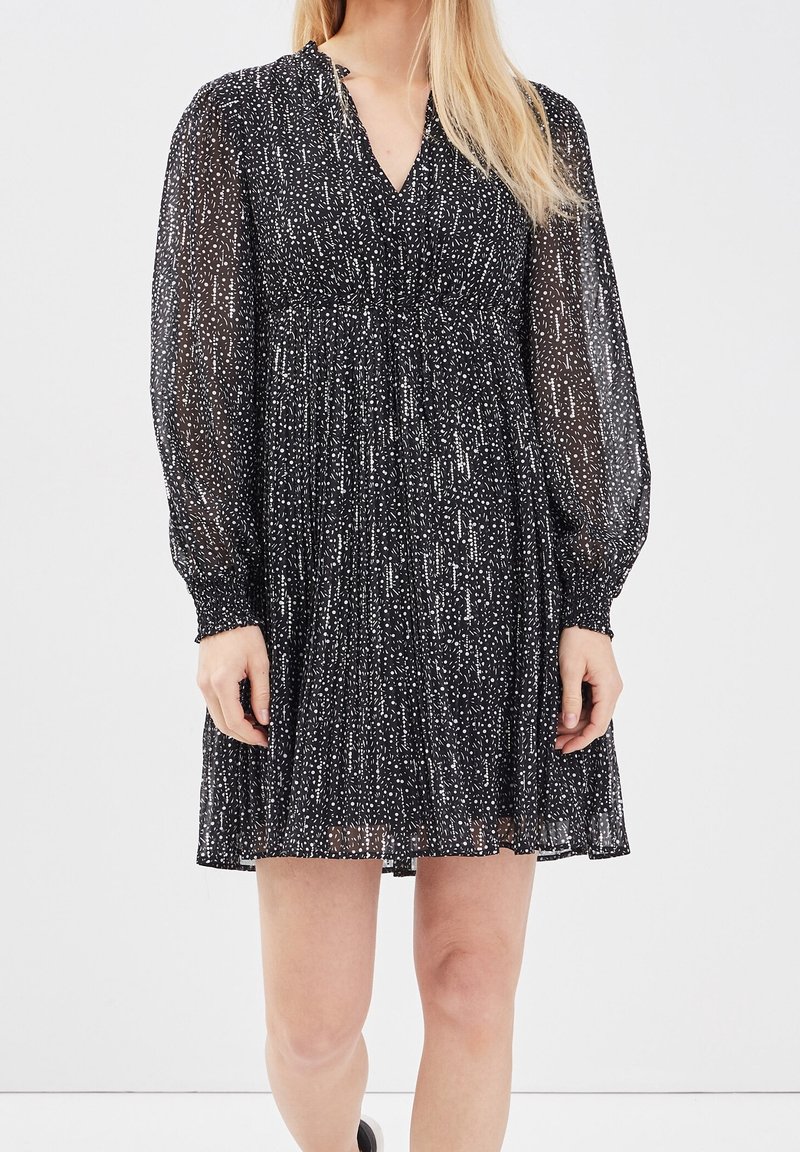 Robe noire avec un motif à taches blanches, design plissé, manches longues et décolleté en V. Fabriquée à partir d'un tissu léger et transparent.