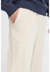 Cotton corduroy pants in cream with vertical ribbing, featuring side pockets and a relaxed fit, paired with a dark blue knitted sweater.