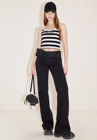 Sorte brede bukser med et matchende bælte, hvid og sort stribet crop top med "MISS SIXTY" logo, og en mønstret sort håndtaske.