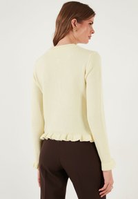 Lichtgele lange mouwen trui met een geruffled zoom en manchetten, met een zachte textuur en een getailleerd ontwerp. Achteraanzicht weergegeven.