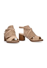Zapatos de tacón abiertos en beige con patrones triangulares recortados, una superficie de ante texturizada y un tacón de bloque de altura media.