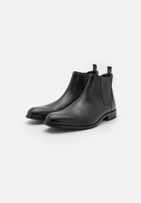 Botas Chelsea de cuero negro con paneles laterales elásticos, puntera redondeada y tiradores en el talón. Textura suave y diseño minimalista.