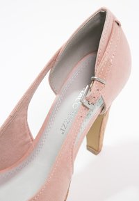 Chaussure à talon haut en suède rose avec un design à bride arrière, détail de boucle en argent et semelle en liège texturé. Doublure intérieure lisse.