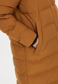 Brun puffjacka med en slät yta, horisontellt kviltat mönster, tryckknappar och sidofickor integrerade i designen.