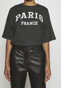 Camiseta gris de gran tamaño con gráfico blanco "PARIS FRANCE", combinada con pantalones de cuero negro de talle alto. Textura suave y corte relajado.