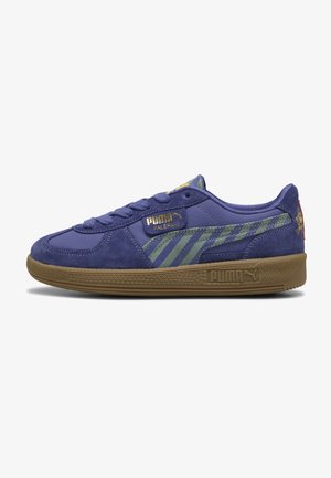 Violet suede ja nahka lenkkarit, joissa on oliivinvihreät raidat, kultaiset logot ja ruskea kumipohja. Varustettu pehmustetulla kauluksella ja nauhakiinnityksellä.