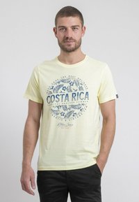 T-shirt jaune à manches courtes avec un graphique tropical en bleu et le texte "COSTA RICA". Tissu doux, col rond, coupe régulière.