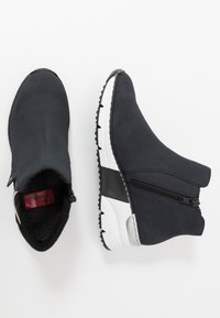 Stivali neri alla caviglia realizzati in materiale morbido con chiusura a zip, suola testurizzata e accentuazione bianca sul tallone. Presentano un design con punta arrotondata.