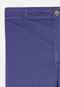 Pantalon slim violet avec une texture lisse, passants de ceinture et un bouton argenté à la taille. Présente des détails cousus le long des coutures.