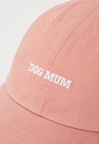 Rózsaszín baseballsapka texturált anyagból, elöl fehér hímzett "DOG MUM" felirattal. Görbült karimával és varrott díszítésekkel.