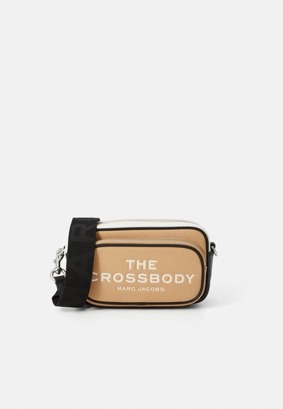 Sac à bandoulière en cuir texturé beige avec des accents noirs. Dispose d'un logo blanc, d'une fermeture éclair et d'une bandoulière noire amovible. Forme rectangulaire.