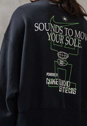 Schwarzer Sweatshirt mit weißem Text „Sounds to Move Your Sole“, einer grünen abstrakten Figur und der Grafik „Powered by Nike Sound Systems 2023“.