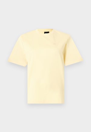 T-shirt jaune pâle à manches courtes et col rond avec un petit logo brodé sur la poitrine gauche, présenté sur un fond gris clair.