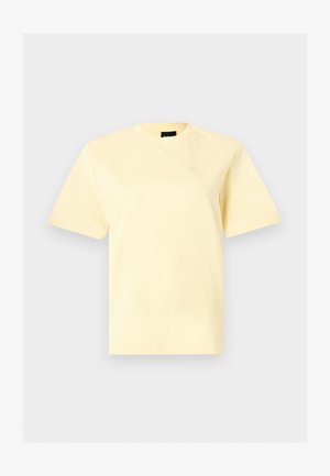 T-shirt jaune pâle à manches courtes et col rond avec un petit logo brodé sur la poitrine gauche, présenté sur un fond gris clair.