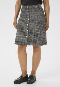 Zwart-witte tweed rok met een rechte snit, voorzien van een voorste knoopsluiting en textuurstof. Draagt met zwarte instappers.
