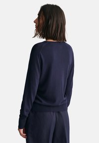 Suéter de punto azul marino con mangas largas, puños y dobladillo acanalados, con cuello redondo y un diseño simple y limpio. Tela texturizada visible.