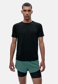 Juodas sportinis marškinėliai su tekstūruotu audiniu, trumpomis rankovėmis ir apykakle, derinami su žaliais šortais su sluoksniuota konstrukcija.