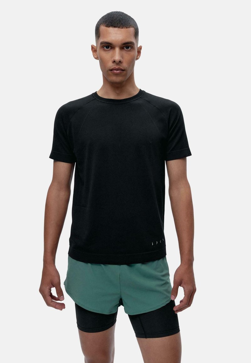 Černé sportovní tričko s texturovanou tkaninou, krátkými rukávy a kulatým výstřihem, doplněné o zelené šortky se zvrstveným designem.